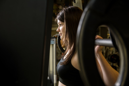 Closeup of a young girl in the gym with a barbell. Woman trains his muscles on the simulator. Fitness, CrossFitの写真素材