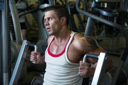 Close-up portrait of a muscular man in the gym. A strong man bodybuilder on a simulator shakes hand muscles. fitness trainingの写真素材