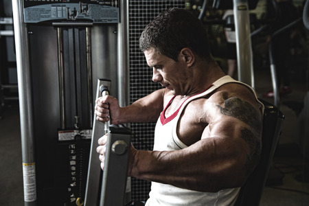 Portrait of a muscular man in the gym. A strong man bodybuilder on a simulator shakes muscles. fitness trainingの写真素材