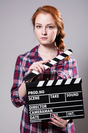 Beautiful red-haired woman holding a movie clapper, isolated over gray backgroundの写真素材