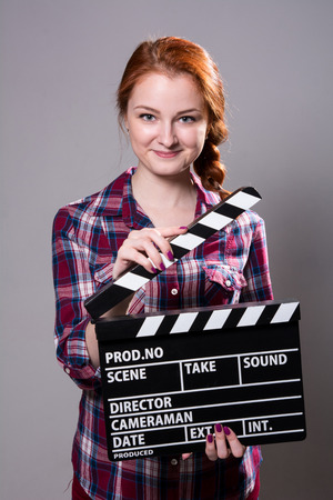 Beautiful smiling red-haired woman holding a movie clapper.の写真素材