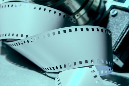 Close-up of old photo camera with metallic color. In the foreground tape 35 mm movie film. toned imageの写真素材