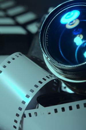 Close-up photo movie camera lens. Roll film cinema in the foreground. Movie clapper in the background as blurringの写真素材