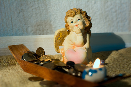 Figurine little angel with a heart who dreams of burning candle on the background of the boat with coinsの写真素材