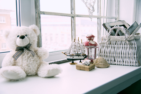 Interior windowsill in a rustic style. Ship with shells of the old lamp and teddy bear wicker basket on a windowsill.の写真素材