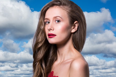 Glamour portrait of beautiful woman model with fresh daily makeup and romantic wavy hairstyle. Fashion shiny highlighter on skin, sexy gloss lips dark eyebrows. Against background of sky relaxationの写真素材