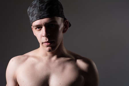 Muscular young sexy man  in a cap with a naked torso on black background