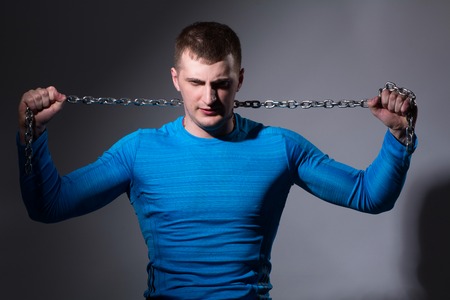 Young man with a tight chain in a blue shirt on a gray backgroundの写真素材