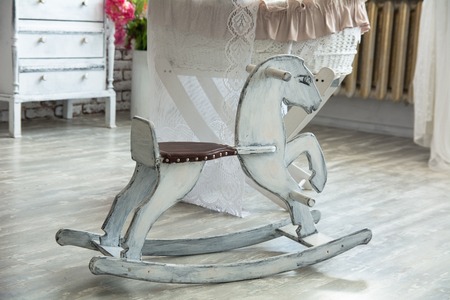 Children's cot with a teddy bear on a background of a brick wall and wooden floor. Children's room in retro style with rocking horseの写真素材