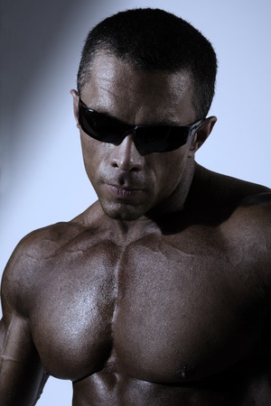 Closeup portrait of a muscular man. Athletic black man naked torso wearing sunglasses in the studio.の写真素材