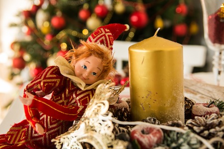 On the festive table cones, candles and doll. Christmas table on the background of trees dressed up in a country houseの写真素材
