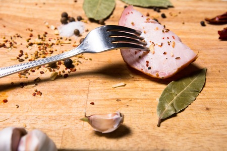 Fork with a slice of bacon on board herbs. Background dried chilli pepper and bay leafの写真素材