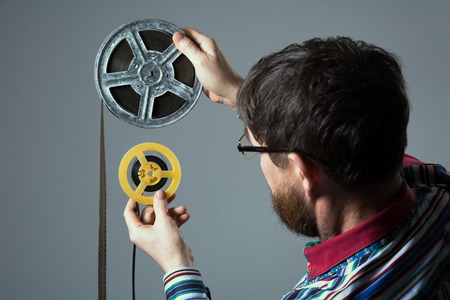 Bearded man watch two film reel 16mm. A man in a striped shirt Glasses assistant directorの写真素材