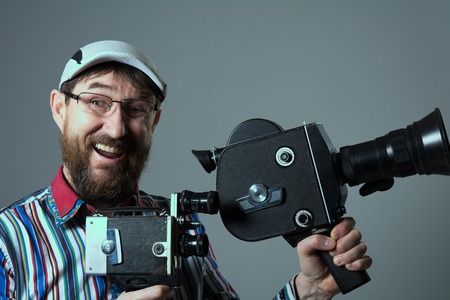 Laughing bearded man two old retro film camera. Man in glasses director cinema operator in glasses...
