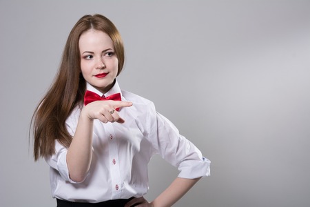 Portrait of a young woman with a butterfly on her neck showing a finger to the side. Isolated on a gray backgroundの写真素材