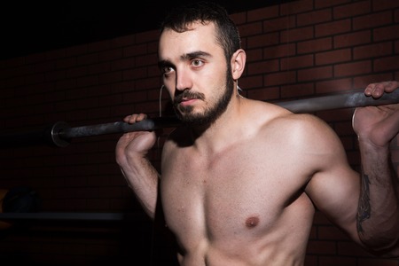 Close-up of a young muscular man with a barbell bar in the gym. Bodybuilder exercising against a...