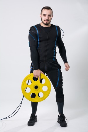 Fitness man in an electric stimulation suit on a white background in studio in full growth. A...