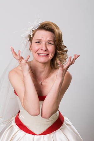 Portrait of an emotional bride in horror. Frustrated woman in a wedding dress on a white backgroundの写真素材