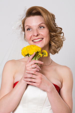 Smiling girl in wedding dress with flowers. Happy bride on a light background with dandelions in the studioの写真素材