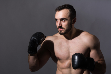 Portrait of a young muscular man in boxing gloves in a pose. Fitness man on a dark background in the studioの写真素材