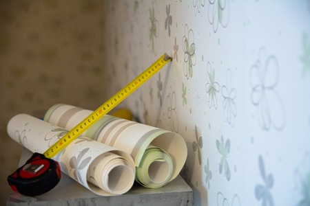 Two rolls of wallpaper and a measuring tape measure lie against the wall with floral wallpaperの写真素材