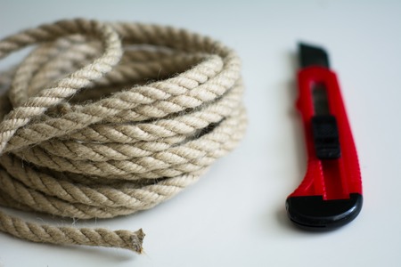 Coarse rope roll and a knife with a red handle on a white surface