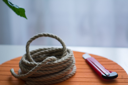 Coarse rope roll and a knife with a red handle against the background of an orange circle and a green leaf of a plantの写真素材