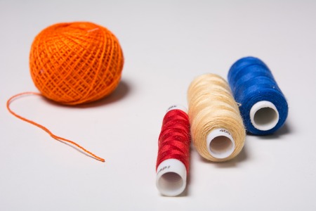 Three coils of multi-colored thread and a hank of orange on a white table.の写真素材