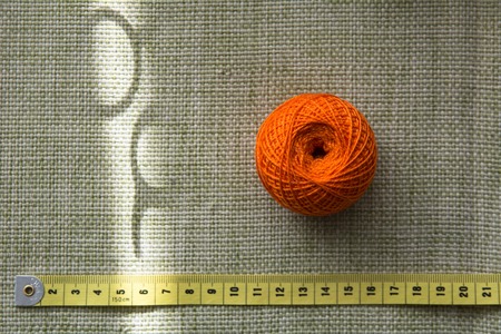 Tangle of orange thread and a measuring tape on a green cloth. The scissors' shadow against the...