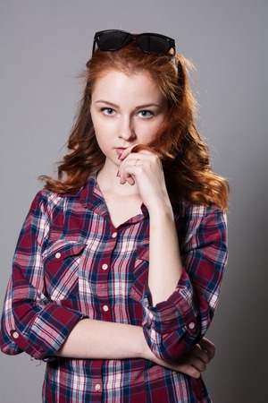 Portrait of a girl with sunglasses on her head looking at the camera. Red-haired woman in plaid shirt isolated on gray backgroundの写真素材