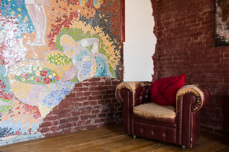 Interior of the room with an old leather armchair and a brick wall. Multicolored mosaic on the wallの写真素材