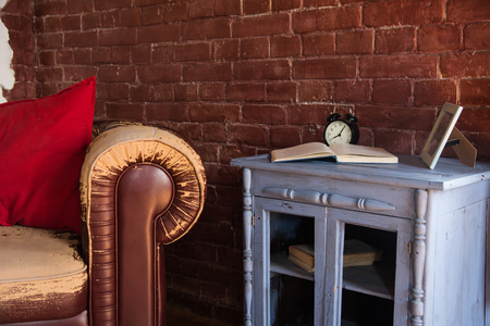 An old brown armchair and a clock with a book on a wooden buffet.の写真素材