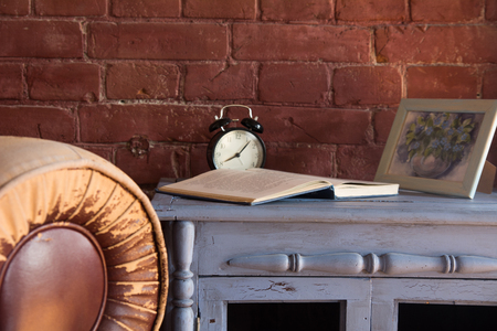 Desk clock with a book on a wooden cupboard against a brick wall background.の写真素材