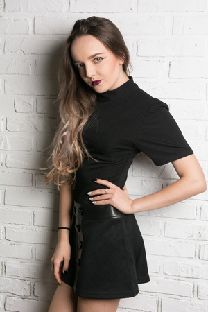 Portrait of a young beautiful woman on brick wall background. Girl with long hair with hand on waistの写真素材