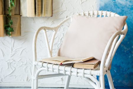 Wicker chair with a pillow and books. Background with books on the wall and flowersの写真素材