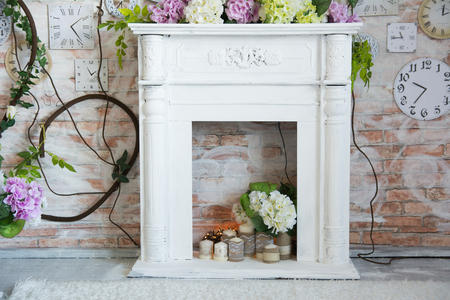 White decorative fireplace with flowers and candles. Background wall with clock and rosesの写真素材