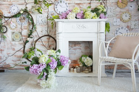 Interior design of a room with a fireplace and a clock on the wall. Wicker chair with flowers in a vaseの写真素材