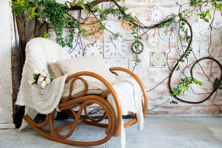 Background with rocking chair with pillows on the background of branches with flowers and wall clocks. Rustic interior backgroundの写真素材