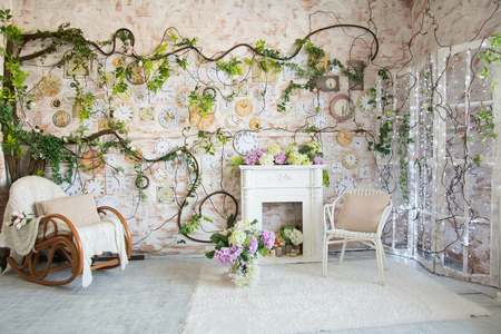 Interior design of a room with a fireplace and a clock on the wall. Wicker chair and chair with a blanket of flowers in a vaseの写真素材