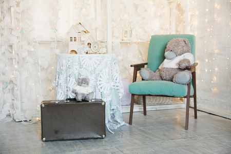 Teddy bear on an old chair and a toy house with clock on the tableの写真素材