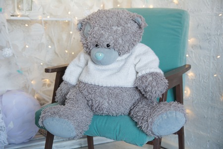 Teddy bear sitting in an old green armchair. Bear in a bright room on the background of the lights of the garlandの写真素材