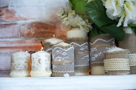 Paraffin candles with a bouquet of white artificial flowers on a brick wall background.の写真素材