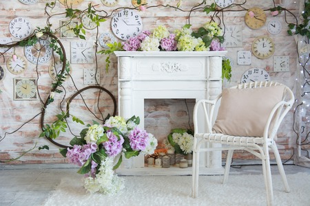 Interior design of a room with a fireplace and a clock on the wall. Wicker chair with flowers in a vaseの写真素材