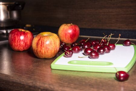Apples and cherries on a cutting board. Background fruits on the kitchen tableの写真素材
