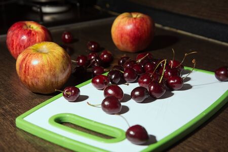 Apples and cherries on a cutting board. Background fruits on the kitchen tableの写真素材