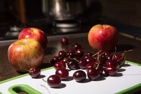 Background apples and cherries on a cutting board. Fruit on the kitchen tableの写真素材