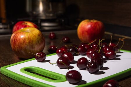 Background apples and cherries on a cutting board. Fruit on the kitchen tableの写真素材