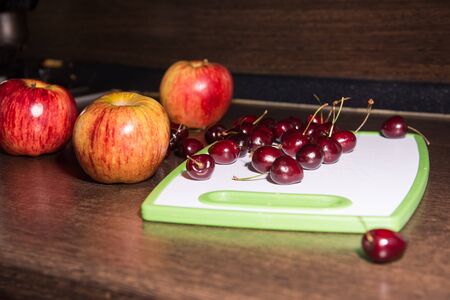 Background apples and cherries on a cutting board. Fruit on the kitchen tableの写真素材