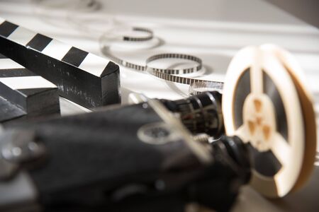Unwound narrow retro film on a light reel against the background of an old movie camera and a movie clapper. Cinema movie accessoriesの写真素材