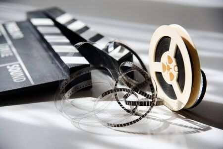 Unwound narrow retro film strip on a light reel with a movie clapperboard. Cinema movie accessoriesの写真素材